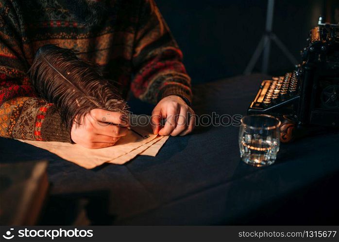 Male hands writes with a feather on vintage paper. Dark blue table cloth on background. Male hands writes with a feather on vintage paper