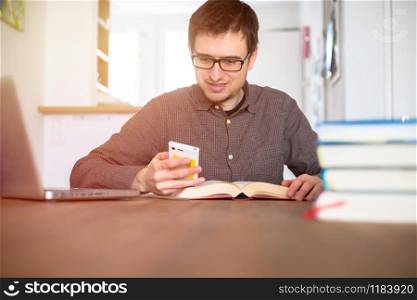 Male happy student researching and learning at home, stack of books blurry