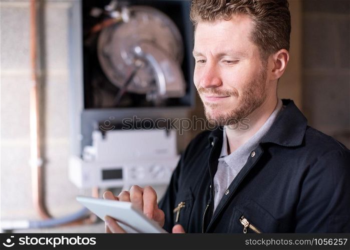 Male Heating Engineer Servicing Central Heating Boiler Using Digital Tablet