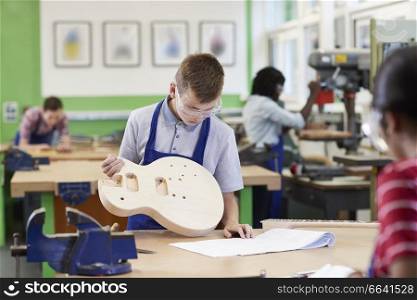 Male High School Student Building Guitar In Woodwork Lesson