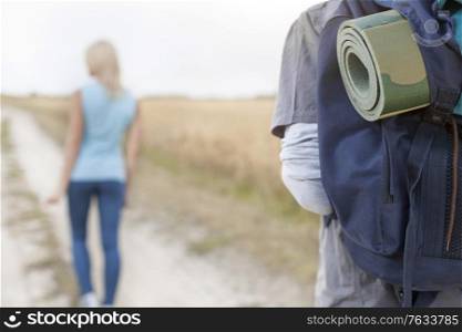 Male hiker carrying backpack with woman walking in foreground on field