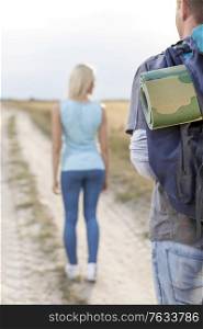 Male hiker carrying backpack with woman walking in foreground on field