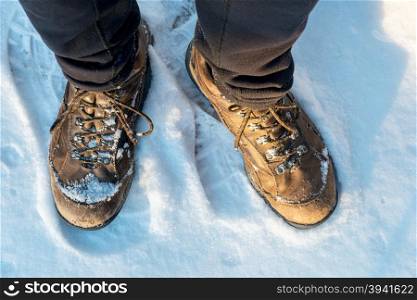 male hiker feet in old hiking boots on a snowy trail, top view