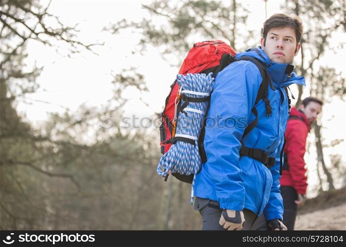 Male hiker looking away with friend in background at forest