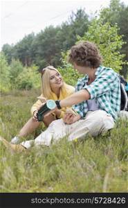 Male hiker pouring coffee for woman while relaxing in field