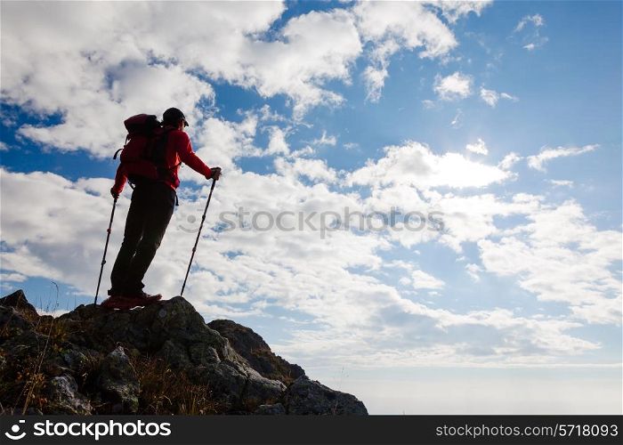 Male hiker standing on the top of a mountain. Summer day with shiny sun. Rear view.