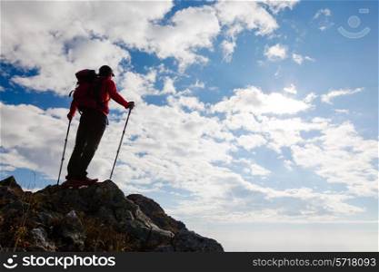 Male hiker standing on the top of a mountain. Summer day with shiny sun. Rear view.