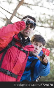 Male hiker using binoculars while friend showing him something in forest