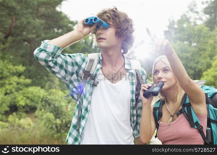 Male hiker using binoculars while woman showing him something in forest