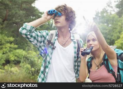 Male hiker using binoculars while woman showing him something in forest