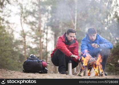 Male hikers warming hands at campfire in forest
