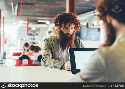 Male hipster twins working on laptop at office desk