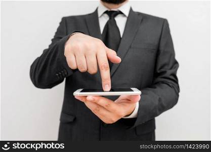 Male human wear formal work suit hold smart hi tech smartphone use one hand. Male human with beard wear formal working clothes hold high technology smartphone device. Man dressed in work suit plus tie holding small mobile hi tech phone using one hand