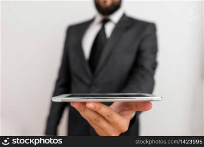 Male human wear formal work suit hold smart hi tech smartphone use one hand. Male human with beard wear formal working clothes hold high technology smartphone device. Man dressed in work suit plus tie holding small mobile hi tech phone using one hand
