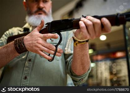 Male hunter reloads rifle in gun store. Weapon shop interior, ammo and ammunition assortment, firearms choice, shooting hobby and lifestyle. Male hunter reloads rifle in gun store