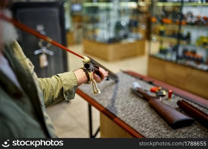 Male hunter with ramrod cleans rifle in gun store. Weapon shop interior, ammo and ammunition assortment, firearms choice, shooting hobby and lifestyle. Male hunter with ramrod cleans rifle in gun store