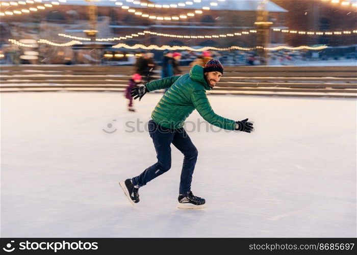 Male in speed demonstrates his skills of skating, has fun on ring, feels sure and confident on ice, spends free time outdoor, enjoys winter vacations, being photographed in movement