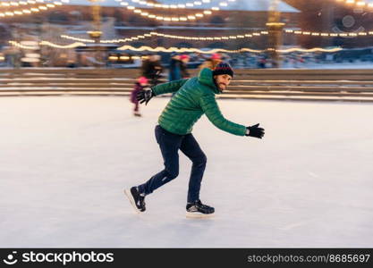 Male in speed demonstrates his skills of skating, has fun on ring, feels sure and confident on ice, spends free time outdoor, enjoys winter vacations, being photographed in movement