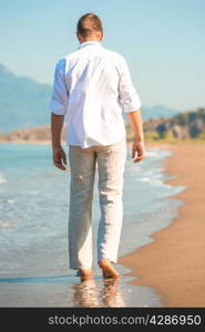 male in white clothing walking along the beach