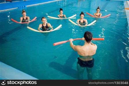 Male instructor and female group, aqua aerobics training in the pool. Man and women in the water, sport swimming fitness workout. Instructor and female group, training in the pool