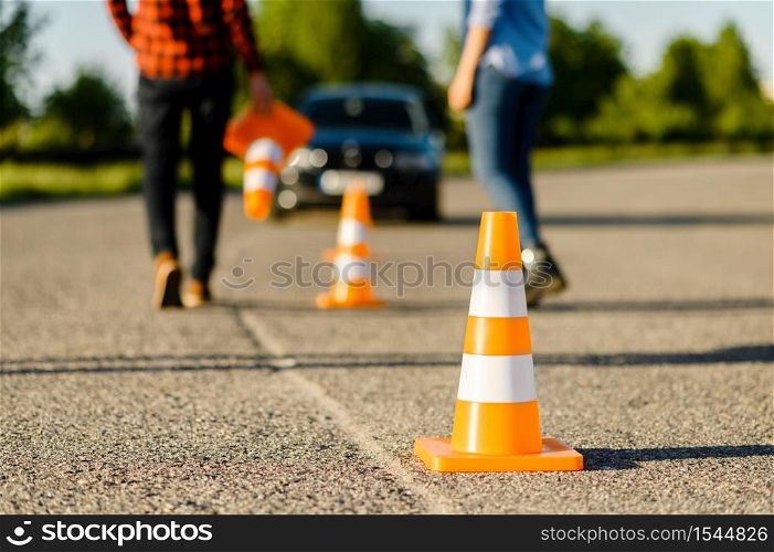 Male instructor and female student on road with traffic cones, lesson in driving school. Man teaching lady to drive vehicle. Driver&rsquo;s license education. Instructor and student on road with traffic cones