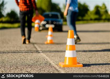 Male instructor and female student on road with traffic cones, lesson in driving school. Man teaching lady to drive vehicle. Driver&rsquo;s license education. Instructor and student on road with traffic cones