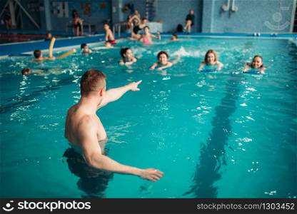 Male instructor works with female class on workout in swimming pool. Aqua aerobics training, water sport. Instructor works with class in swimming pool