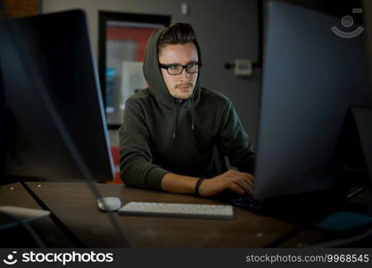 Male internet hacker in hood and glasses sitting at monitors. Illegal web programmer at workplace, criminal occupation. Data hacking, cyber security. Male internet hacker in hood and glasses