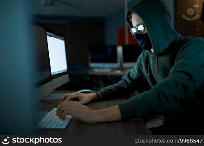 Male internet hacker in hood holds laptop, front view. Illegal web programmer at workplace, criminal occupation. Data hacking, cyber security. Male hacker in hood holds laptop, front view