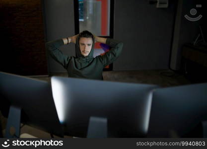 Male internet hacker in hood leisures at monitors. Illegal web programmer at workplace, criminal occupation. Data hacking, cyber security. Male internet hacker in hood leisures at monitors