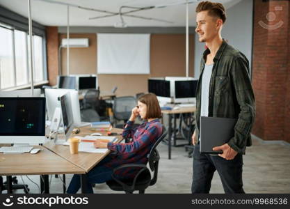 Male IT specialist holds laptop in office. Web programmer or designer at workplace, creative occupation. Modern information technology, corporate team. Male IT specialist holds laptop in office