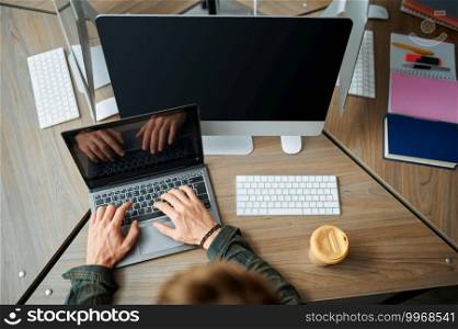 Male IT specialist works on laptop in office, top view. Web programmer or designer at workplace, creative occupation. Modern information technology, corporate team. IT specialist works on laptop in office, top view