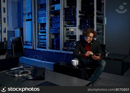 Male IT technician working in server room with tablet. Man engineer near racks with computer equipment. Male IT technician working in server room with tablet