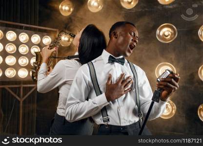Male jazz performer and female saxophonist with saxophone, performing on the stage with spotlights. Jazz players playing on the scene. Male jazz performer and female saxophonist