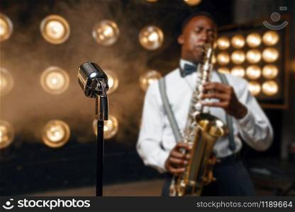 Male jazz performer plays the saxophone on the stage with spotlights. Black jazzman preforming on the scene. Male jazz performer plays the saxophone on stage