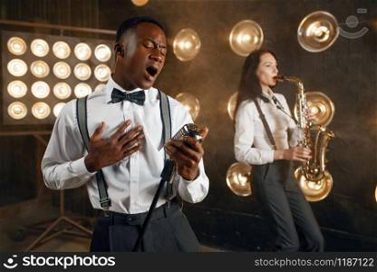 Male jazzman and female saxophonist with saxophone on the stage with spotlights. Jazz performers playing on the scene. Male jazzman and female saxophonist with saxophone
