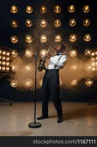 Male jazzman plays the saxophone on the stage with spotlights. Black jazz musician preforming on the scene. Male jazzman plays the saxophone on stage