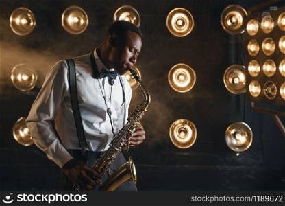Male jazzman plays the saxophone on the stage with spotlights. Black jazz musician preforming on the scene