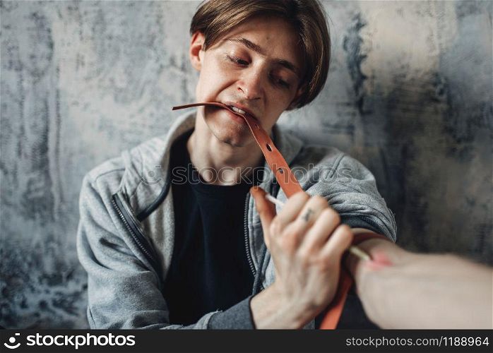 Male junkie with a syringe doing an injection dose in the arm. Narcotic addiction concept, drug addicted people. Male junkie with syringe doing an injection dose