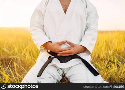 Male karate fighter sitting on the ground in summer field. Martial art training outdoor. Male karate fighter sitting on the ground in field