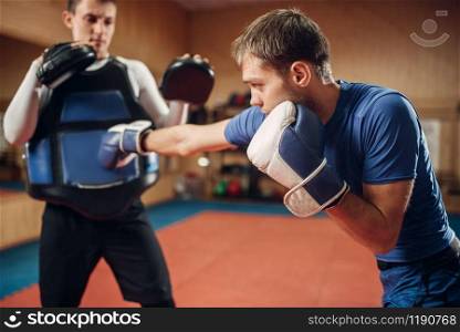 Male kickboxer in gloves practicing hand punch with a personal trainer in pads, workout in gym. Boxer on training, kickboxing practice. Male kickboxer in gloves practicing hand punch