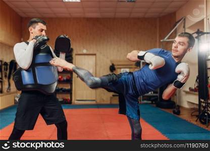 Male kickboxer practicing kicking with a personal trainer, workout in gym. Boxer strikes on training, kickboxing practice. Kickboxer practicing kicking with personal trainer