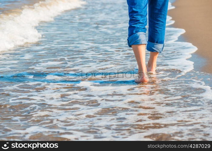 male legs in jeans walking along the sandy seashore