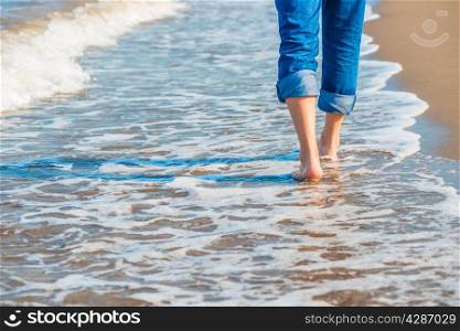 male legs in jeans walking along the sandy seashore