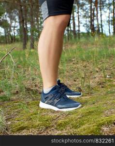 male legs of athlete runner in blue shoes in the middle of the forest, summer day