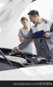 Male maintenance engineer explaining car engine to female customer in repair shop