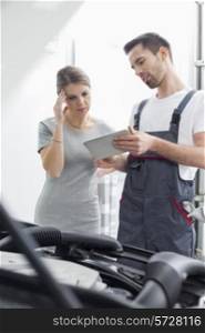 Male maintenance engineer showing digital tablet to worried customer at workshop