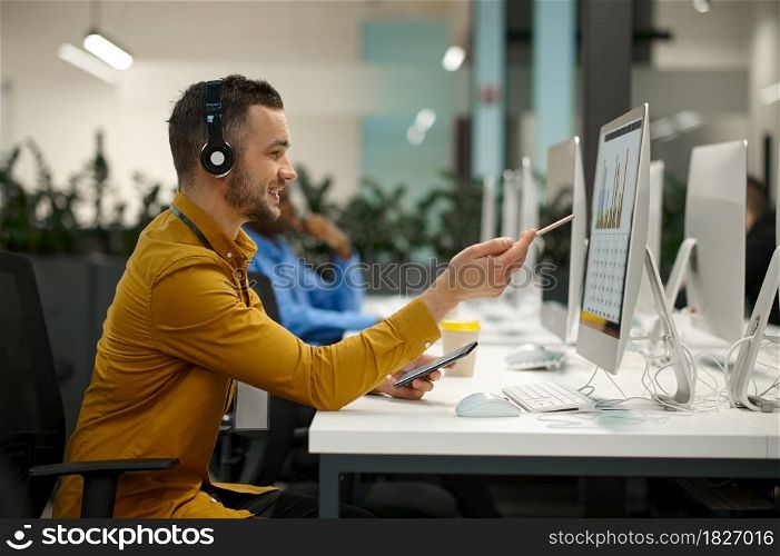 Male manager in headphones on his workplace, idea developing in IT office. Professional worker, planning or brainstorming. Successful businessman works in modern company. Male manager in headphones, workplace in IT office