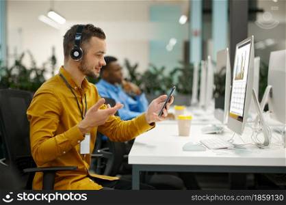Male manager in headphones on his workplace, idea developing in IT office. Professional worker, planning or brainstorming. Successful businessman works in modern company. Male manager in headphones, workplace in IT office