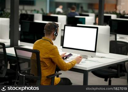 Male manager in headphones works on computer, idea developing in IT office. Professional worker, planning or brainstorming. Successful businessman works in modern company. Manager in headphones works on computer, IT office